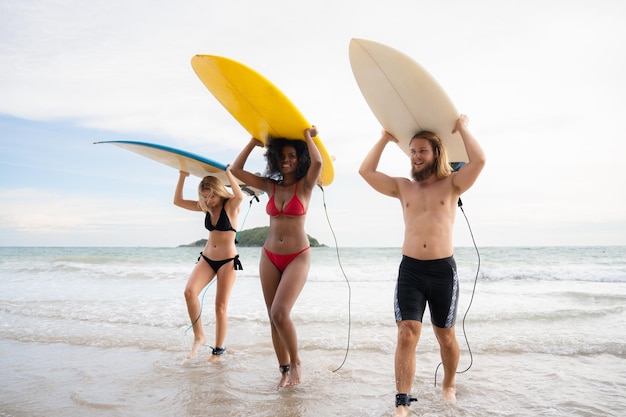 Vista posteriore di due donne e un giovane che tengono le tavole da surf in testa e camminano in mare per fare surf