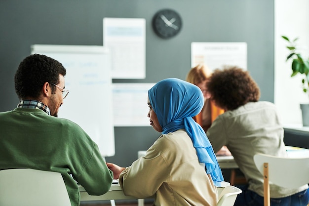 Vista posteriore di due giovani studenti interculturali che discutono di un nuovo argomento