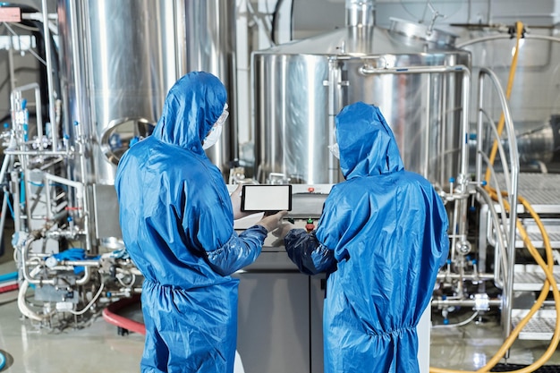 Vista posteriore di due lavoratori che utilizzano il pannello di controllo in una fabbrica chimica