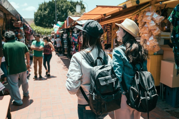 vista posteriore di due ragazze asiatiche migliori amiche viaggiano insieme a los angeles durante le vacanze estive. giovani donne turista zaino in spalla shopping nel mercato all'aperto del messico. donne che camminano in olvera street divertendosi.