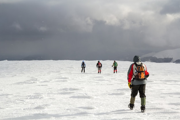 Vista posteriore di escursionisti che camminano sulla collina coperta di neve nelle montagne invernali.