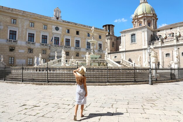 Vista posteriore di giovane bella donna che cammina vicino alla monumentale Fontana Pretorio a Palermo, Italia