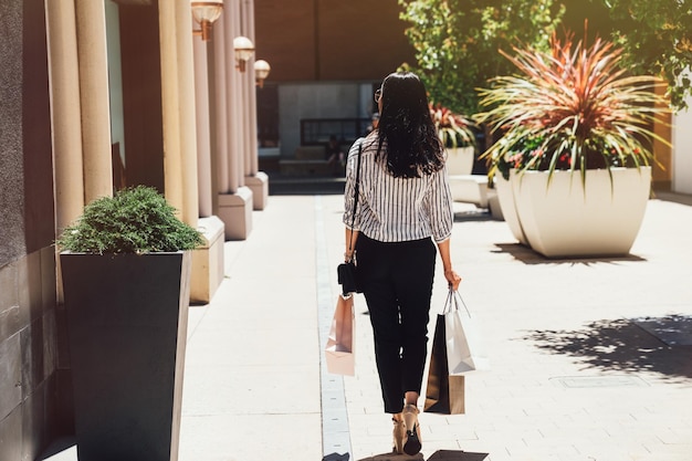 vista posteriore di giovane bella ragazza che cammina tenendo le borse della spesa in una giornata di sole all'aperto. signora asiatica in acquisti casuali intelligenti nella vendita di Natale il giorno di Santo Stefano. donna con i capelli lunghi neri nel centro commerciale del centro.