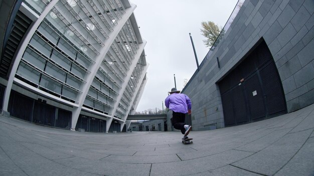 Vista posteriore di hipster sportivo che guida skateboard all'aperto al rallentatore Ragazzo skater attivo che fa trucco estremo con skate in strada cittadina Giovane skateboarder che cade durante la lezione fuori