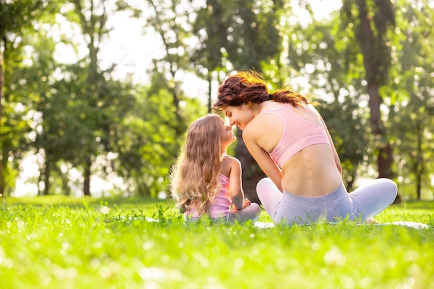 Vista posteriore di madre e figlia in abbigliamento sportivo seduti sul tappetino da yoga naso a naso