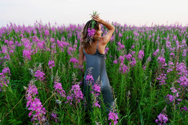 Vista posteriore di stare giovane donna bionda in abito grigio e in possesso di un mazzo di fiori sul prato fireweed