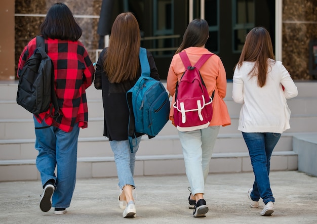 Vista posteriore di un gruppo di quattro giovani studenti universitari attraenti ragazze asiatiche che camminano insieme nel campus universitario. Concetto per l'istruzione, l'amicizia e la vita degli studenti universitari.