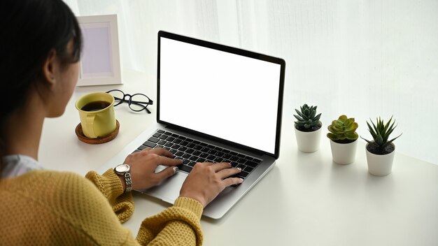 Vista posteriore di un libero professionista giovane donna felice sta lavorando e digitando SMS sul computer portatile.