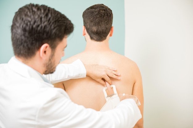 Vista posteriore di un medico che misura il grasso corporeo e le pieghe sulla schiena di un paziente in una clinica sanitaria