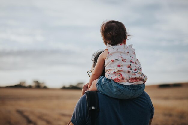 Vista posteriore di un padre che porta la figlia sulle spalle contro il cielo