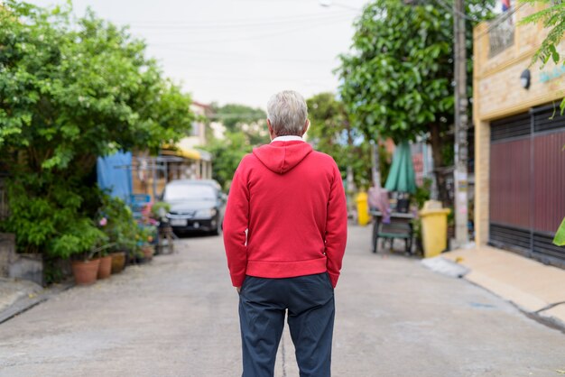 Vista posteriore di un uomo anziano in piedi mentre indossa la giacca rossa all'aperto