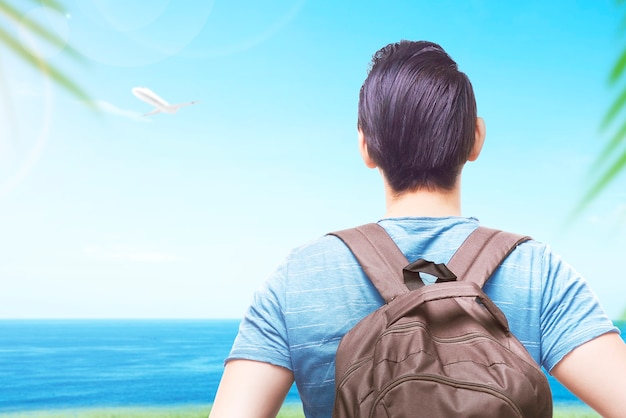 Vista posteriore di un uomo asiatico con uno zaino che guarda la vista sull'oceano con una vista del cielo blu