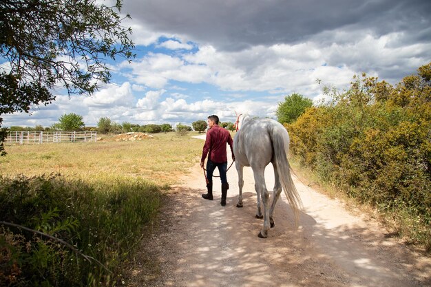 Vista posteriore di un uomo che cammina con un cavallo su una strada di terra contro il cielo