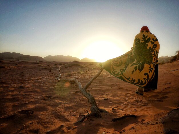 Vista posteriore di un uomo che cammina nel deserto contro il cielo durante il tramonto