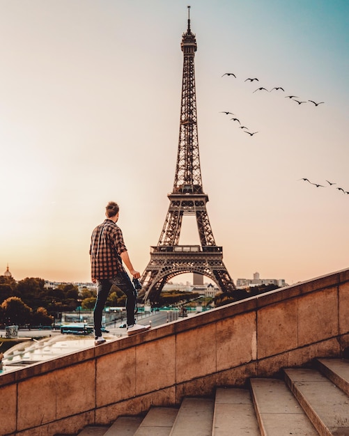 Vista posteriore di un uomo che guarda la Torre Eiffel mentre sta in piedi su una ringhiera contro il cielo durante il tramonto