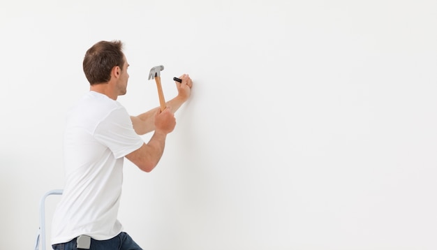 Vista posteriore di un uomo che martella contro un muro bianco