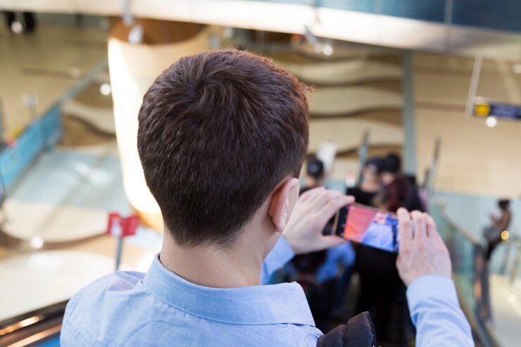 Foto vista posteriore di un uomo che scatta foto con il cellulare all'aeroporto