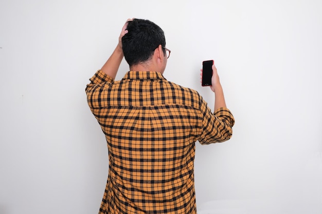 Vista posteriore di un uomo che si gratta la testa quando guarda il suo telefono cellulare