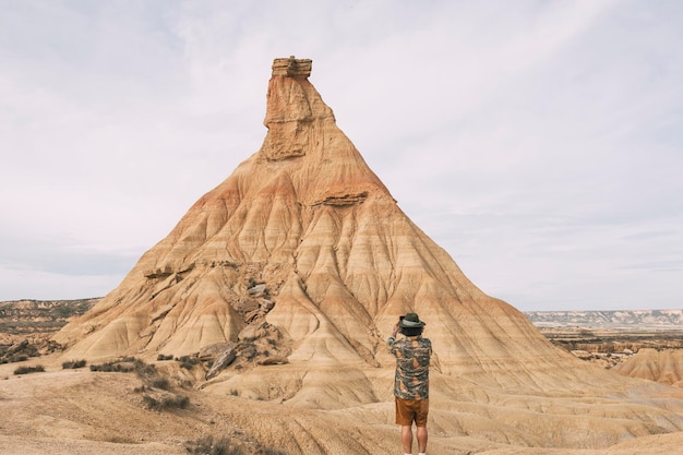 Vista posteriore di un uomo con un cappello che scatta una foto con uno smartphone nel deserto di Bardenas, in Navarra