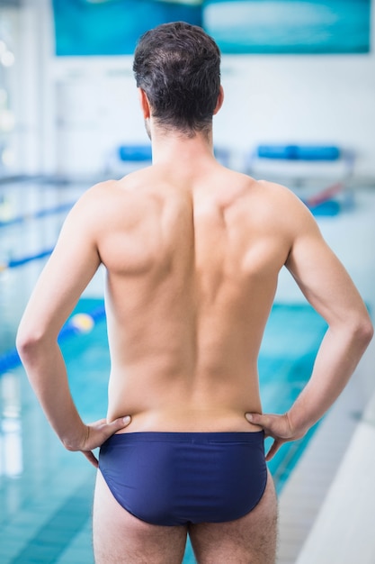 Vista posteriore di un uomo in forma con le mani sui fianchi in piscina
