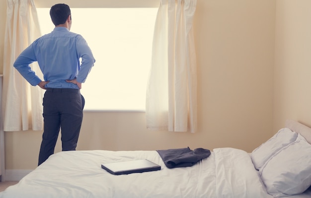 Vista posteriore di un uomo in piedi davanti a una finestra e guardando fuori