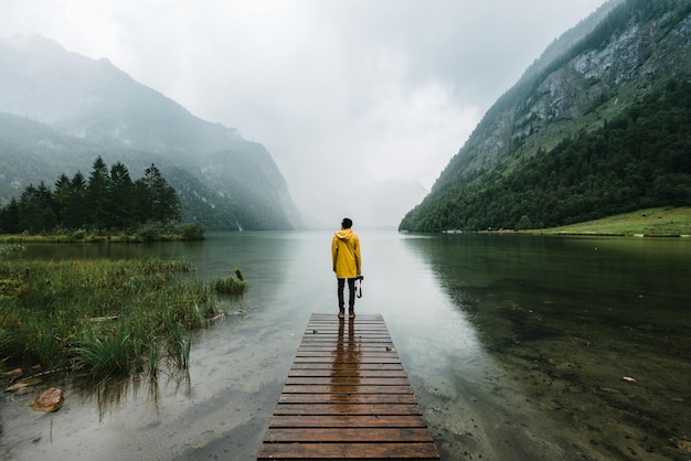 Vista posteriore di un uomo in piedi sul molo sul lago contro le montagne