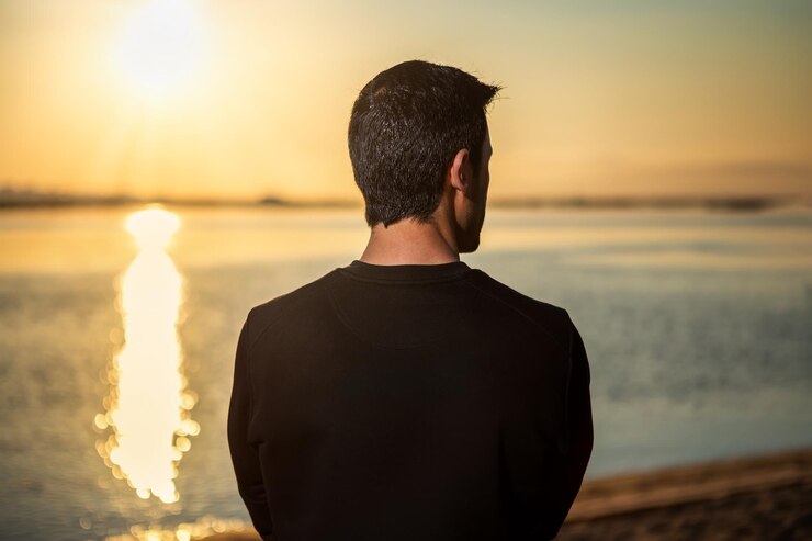 Foto vista posteriore di un uomo in piedi sulla spiaggia durante il tramonto