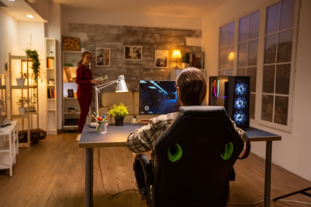 Vista posteriore di un videogiocatore professionista che gioca su un potente PC a tarda notte nel soggiorno.