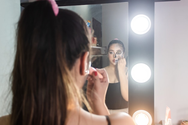 Vista posteriore di una bella ragazza che sbava il trucco di Halloween nella sua camera da letto.