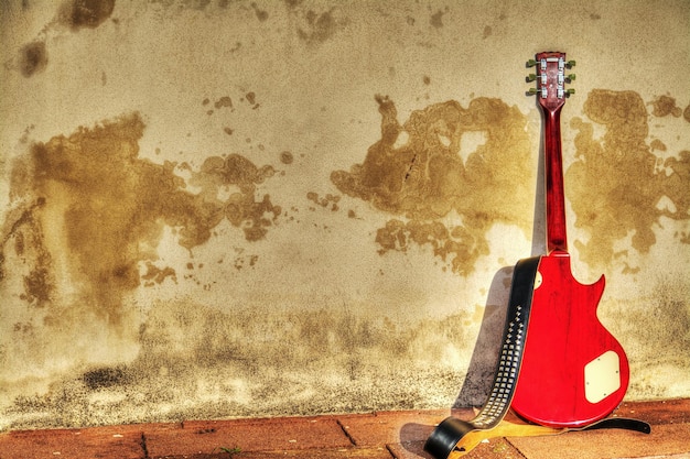 Vista posteriore di una chitarra elettrica appoggiata su una parete rustica in mappatura dei toni hdr