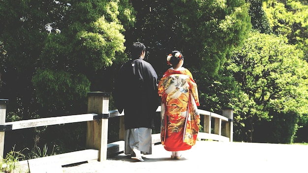 Vista posteriore di una coppia in abiti tradizionali che cammina su un ponte pedonale vicino agli alberi