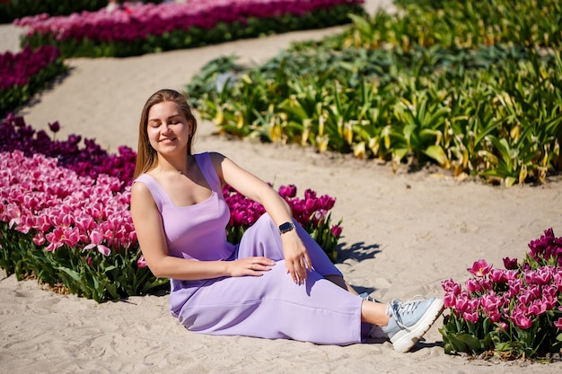 Vista posteriore di una donna anonima in abito estivo e cappello che cammina vicino a tulipani in fiore nel prato in una giornata di sole nella natura