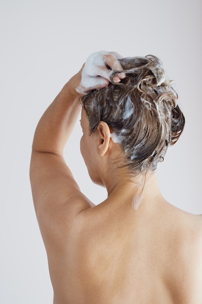 Vista posteriore di una donna anziana con le spalle nude che lava i capelli con lo shampoo