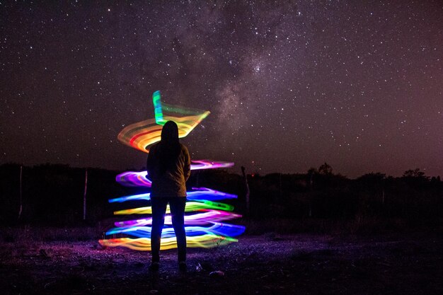 Vista posteriore di una donna che guarda una pittura a luce colorata contro il campo stellato di notte