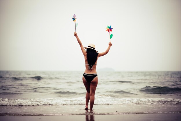 Vista posteriore di una donna che tiene dei giocattoli a ruota mentre cammina sulla spiaggia