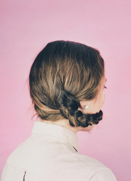 Vista posteriore di una donna con i capelli intrecciati intorno alla faccia contro la parete rosa