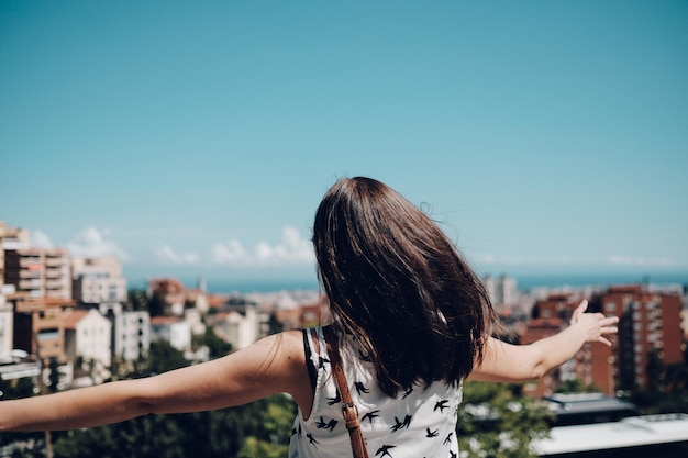 Vista posteriore di una donna con le braccia distese che guarda il paesaggio cittadino contro il cielo