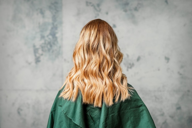 Vista posteriore di una donna con lunghi capelli castani su uno sfondo grigio.