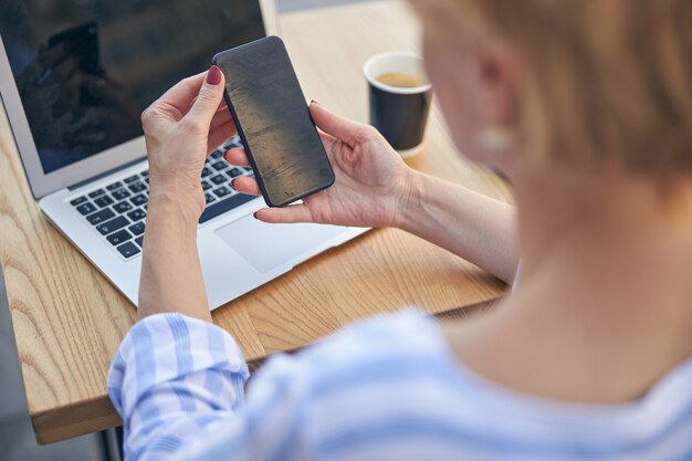 Vista posteriore di una donna con un taglio di capelli corto che tiene il cellulare con entrambe le mani