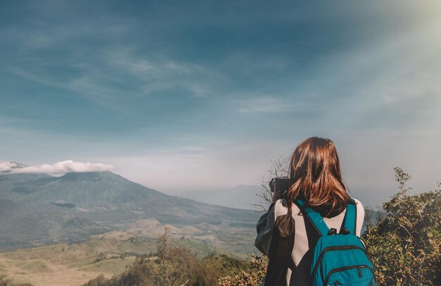 Vista posteriore di una donna con uno zaino che fotografa le montagne in piedi contro il cielo