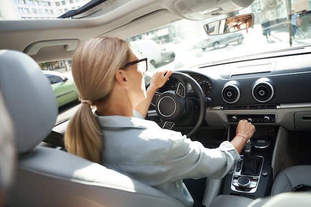 Vista posteriore di una donna d'affari caucasica di successo alla guida della sua auto moderna attraverso la città