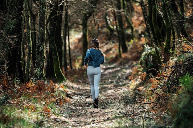 Vista posteriore di una donna in forma irriconoscibile in abbigliamento sportivo che corre lungo il sentiero nella foresta verde