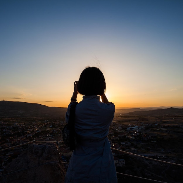 Vista posteriore di una donna in piedi in un punto di osservazione contro un cielo limpido al tramonto.