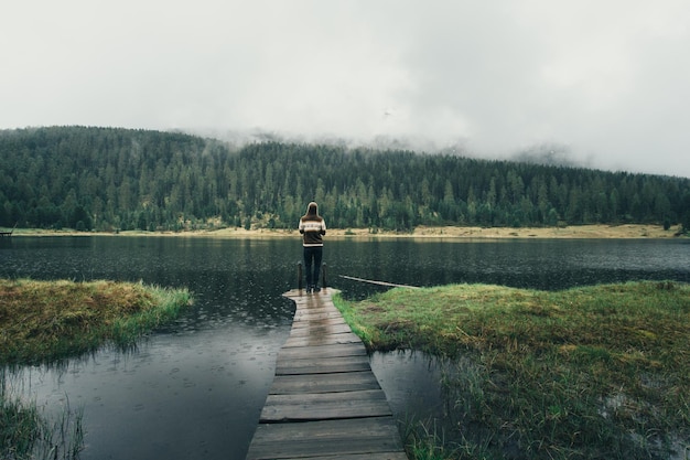 Vista posteriore di una donna in piedi sul molo nel lago contro il cielo durante la pioggia