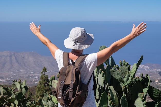 Vista posteriore di una donna matura spensierata a Tenerife che porta uno zaino e si gode una giornata di trekking in cima alla montagna