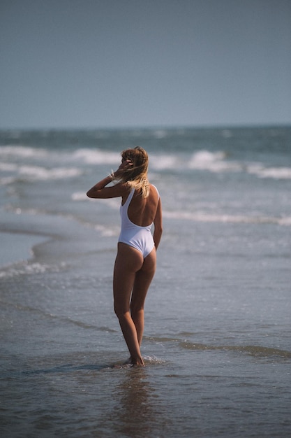 Vista posteriore di una donna seducente che indossa un costume da bagno in un pezzo mentre è in piedi sulla riva in spiaggia