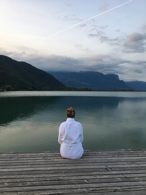 Vista posteriore di una donna seduta sul molo sopra il lago