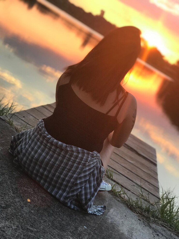 Foto vista posteriore di una donna seduta sul molo vicino al lago contro un cielo arancione