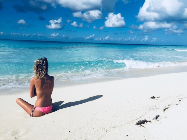 Vista posteriore di una donna seduta sulla spiaggia contro il cielo