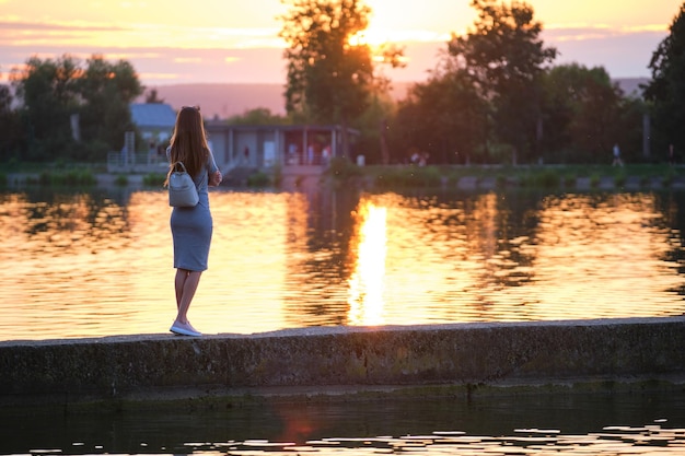 Vista posteriore di una donna sola in piedi sul lato del lago in una calda serata Concetto di solitudine e relax
